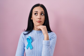 Hispanic woman wearing blue ribbon serious face thinking about question with hand on chin,...