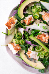 Salad with avocado, pear, cucumber, soft cheese and arugula served on the ceramic plate. Top view