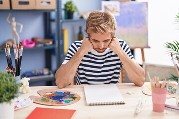 Young man artist sitting on table with worried expression at art studio