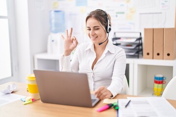 Obraz na płótnie Canvas Young blonde woman wearing call center agent headset doing ok sign with fingers, smiling friendly gesturing excellent symbol