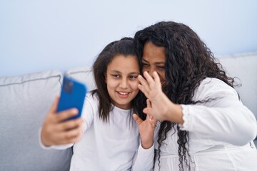 Mother and daughter having video call sitting on sofa at home