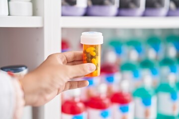 Young beautiful hispanic woman pharmacist holding pills bottle at pharmacy