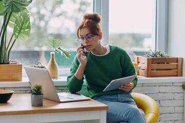 Concentrated young woman talking on mobile phone while working from home
