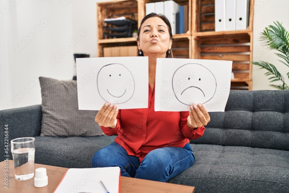 Poster Middle age hispanic woman working on depression holding sad to happy emotion paper looking at the camera blowing a kiss being lovely and sexy. love expression.