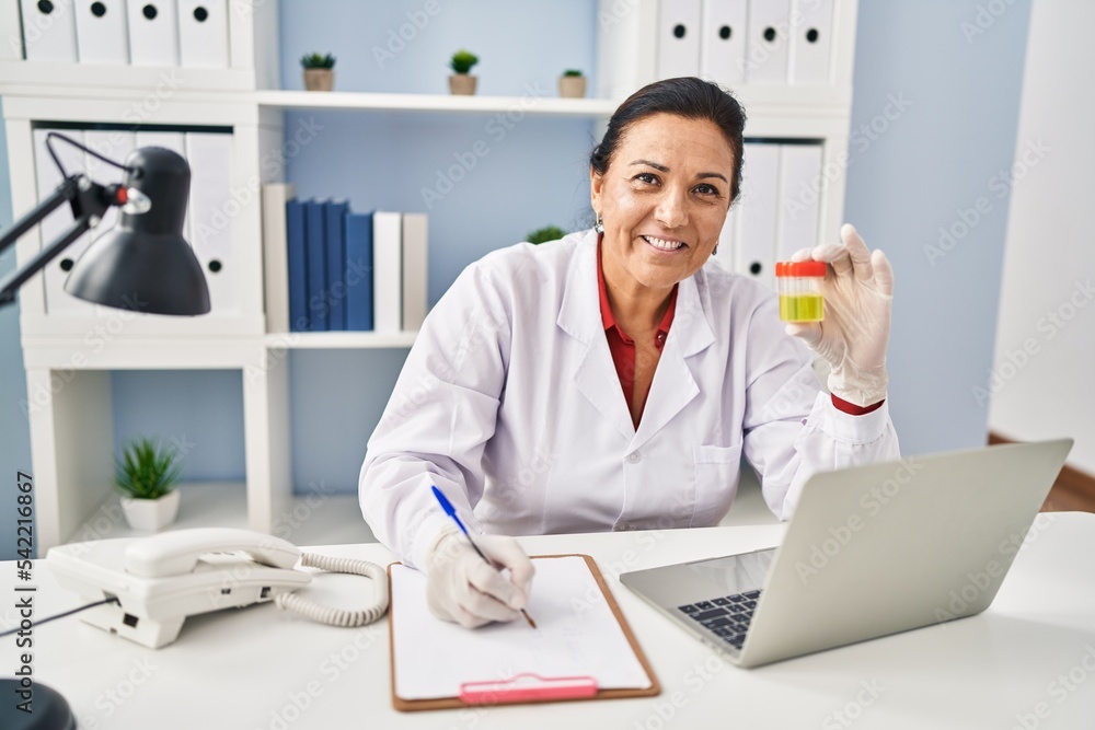 Poster middle age hispanic woman wearing doctor uniform holding urine test tube at clinic