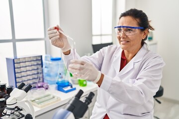 Middle age hispanic woman wearing scientist uniform using pipette at laboratory