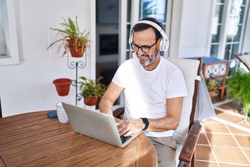 Middle age man using laptop and headphones at terrace home