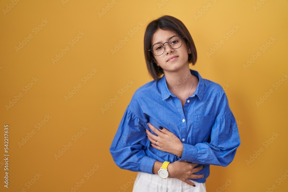 Sticker young girl standing over yellow background with hand on stomach because indigestion, painful illness