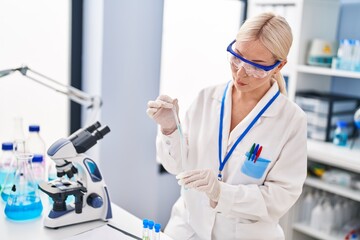 Young blonde woman wearing scientist uniform measuring liquid at laboratory