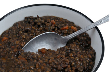 Assiette de lentilles cuisinées avec une cuillère en gros plan sur fond blanc