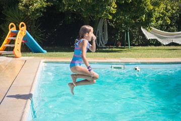 Side view of little Caucasian girl jumping into pool. Fair-haired girl training jumps into water...