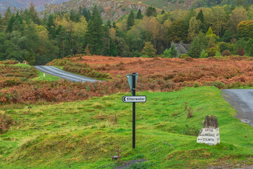 Elterwater in the English Lake District, signpost to the village with vibrant orange and gold colours of Autumn.  Copy space.  Horizontal.