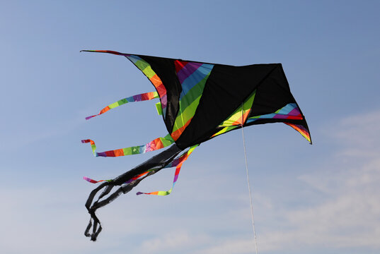 black kite with multicolored rainbow stripes flies high in the blue sky tied to a string