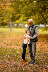 Naklejka na ściany i meble Grandfather spending time with his granddaughter in park on autumn day