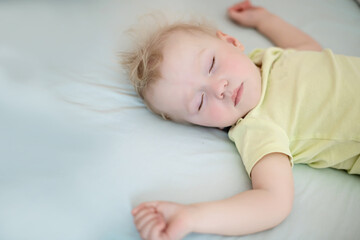 small child sleeps with arms outstretched. girl with blond hair in yellow bodysuit. Concept healthy sleep