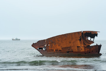 rusty shipwreck against a foggy seascape with a ship in the distance