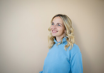 beautiful woman with blond and curly hair standing in front of brown background wearing blue pullover