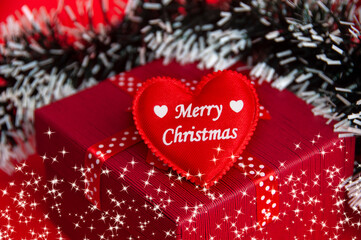 Merry Christmas text on heart shape on top of red color present with Christmas decoration background.