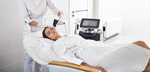 Brunette woman receiving radiofrequency lifting procedure for her face skin rejuvenation at cosmetology center