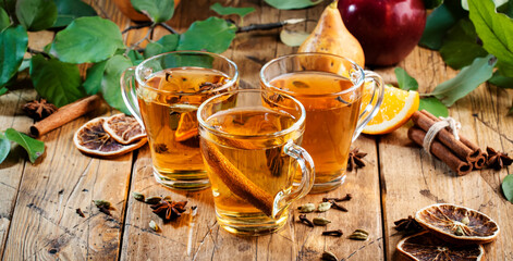 Mulled Cider glass cups: apple, pear and orange flavored  hot cider with spices. Fermented low alcohol cocktail fruit drink on ustic wooden table. Background with leaves