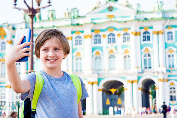 a happy 10 year old boy on an excursion in the center of St. Petersburg takes a selfie, photo, shoots a video on his mobile against the background of the museum, the winter palace Hermitage