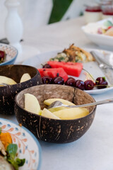 Sliced delicious melon slices in a textured deep wooden bowl. Close-up of bowl full of melons. There are appetizers and ready-made serving plates on the serving table.