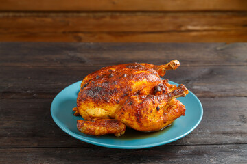 Whole baked chicken carcass with a crust on a blue plate on a wooden table.