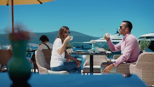A young happy couple have fun chatting over a cup of coffee in a cafe overlooking the yachts and ships background