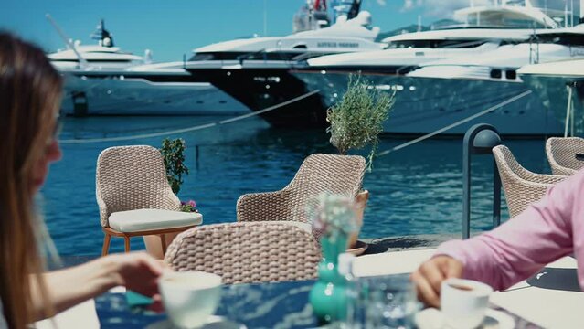 A young happy couple have fun chatting over a cup of coffee in a cafe overlooking the yachts and ships background