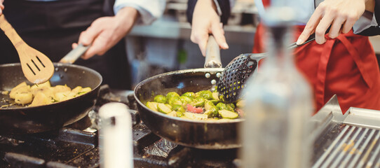 Two diligent chefs working in a hot kitchen cooking delicious food in a pan