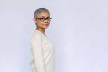 Portrait of confident senior woman wearing eyeglasses and white jumper and looking at camera....
