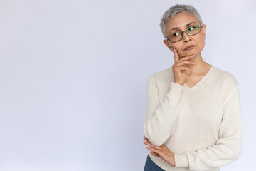 Portrait of thoughtful senior woman wearing eyeglasses and white jumper. Mature Caucasian woman standing with hand on chin and thinking over white background. Planning concept - obrazy, fototapety, plakaty