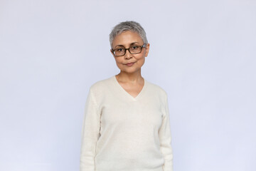 Portrait of serious senior woman wearing eyeglasses and white jumper. Mature Caucasian woman standing and looking at camera over white background. Elderly woman concept - obrazy, fototapety, plakaty