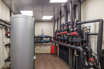Gas boiler room in a private house with a large gray tank, pipe system, pressure gauge, and valve...