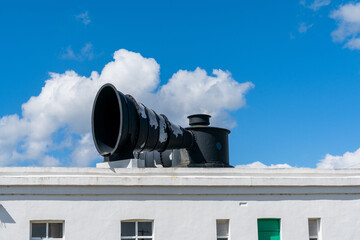 close-up view of a large black metal foghorn on top of the roof of a lighthouse building - obrazy, fototapety, plakaty