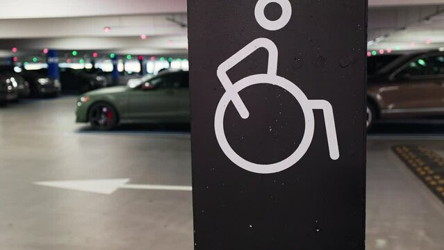 Person walking behind a large disabled sign on a pole in an underground mall parking lot