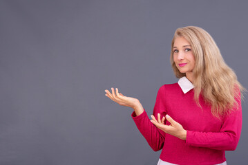 Retrato en plano medio de mujer joven de cabello rubio en actitud positiva señalando con sus manos...