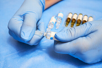 Hands of a nurse in blue gloves open an ampoule with medicine close-up