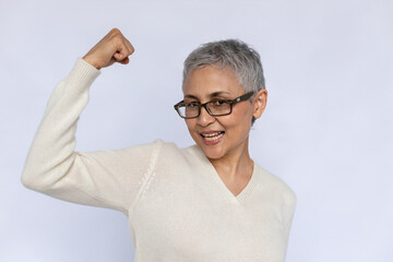 Portrait of happy senior woman showing arm bicep over white background. Confident mature Caucasian...