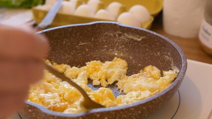 Fried eggs in a pan stirred with fork for hearty meal before hard day's work. With fork, knead eggs in a pan on the stove to make whipped eggs. Cooking food for breakfast at home or in a restaurant.