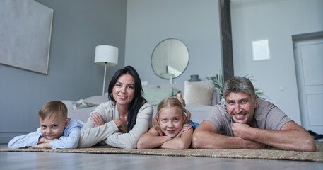 Photo of four members adopted family lying floor toothy smiling fluffy carpet cozy apartments - obrazy, fototapety, plakaty