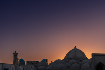 Old Uzbek city skyline with silhouette of big dome and minaret against sunset sky Bukhara Uzbekistan