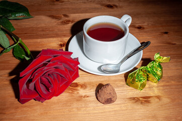 A cup of tea with a teaspoon and a rose. On a wooden table.