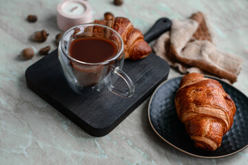 Delicious crispy croissant with chocolate with a cup of invigorating coffee on a light concrete background
