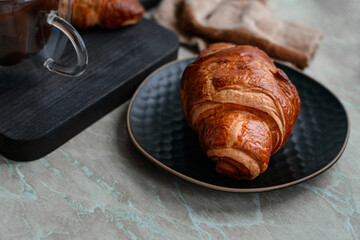 Delicious crispy croissant with chocolate with a cup of invigorating coffee on a light concrete background
