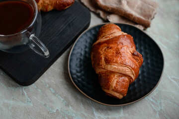 Delicious crispy croissant with chocolate with a cup of invigorating coffee on a light concrete background