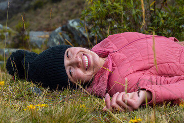 Atractiva mujer tirada en la hierba después de una caminata y sonriendo a la cámara
