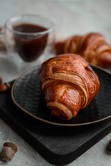 Delicious crispy croissant with chocolate with a cup of invigorating coffee on a light concrete background
