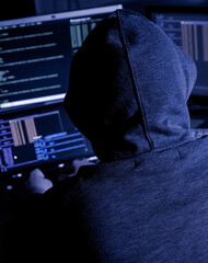 Hooded hacker attempting data breach at night in a dark private office