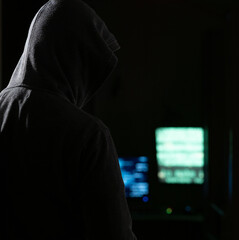 Hooded hacker looming in the dark of a computer room
